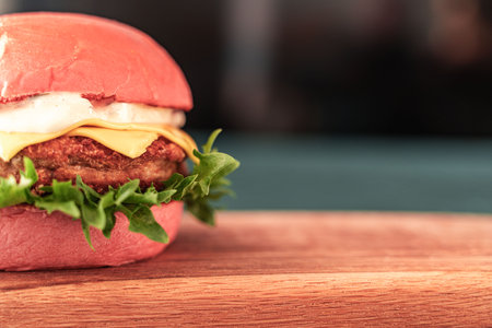 Pink burger with cheese and beef or fish patty with lettuce and sauce on a wooden board and dark background. Close-up. Space for text. High quality photoの写真素材