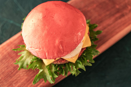Pink burger with cheese and beef or fish patty with lettuce leaves and sauce on a wooden board on a dark background. View from above. Space for the text. High quality photoの写真素材