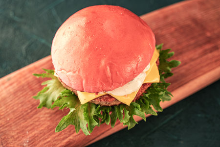 Pink burger with cheese and beef or fish patty with lettuce leaves and sauce on a wooden board on a dark background. View from above. Space for the text. High quality photoの写真素材