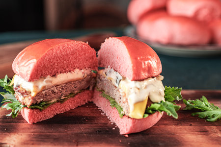 A pink burger with cheese and beef or a fish patty with lettuce leaves and sauce is shown in a section on a wooden board on a dark background. Space for the text. High quality photoの写真素材