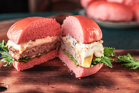A pink burger with cheese and beef or a fish patty with lettuce leaves and sauce is shown in a section on a wooden board on a dark background. Space for the text. High quality photoの写真素材