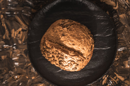 A loaf of rye bread on a black plate on a brown background. Close-up. Top view, space for text. High quality photoの写真素材