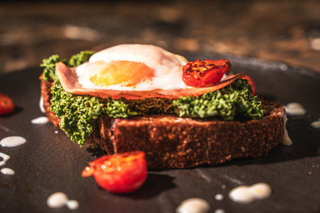 Toasted toast with bacon, poached egg, cherry tomatoes and lettuce on a black mica plate on a dark background. Close-up. High quality photoの写真素材