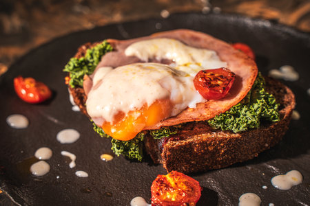 Toasted toast with bacon, poached egg, cherry tomatoes and lettuce on a black mica plate on a dark background. Close-up. High quality photoの写真素材