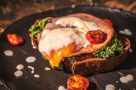 Toasted toast with bacon, poached egg, cherry tomatoes and lettuce on a black mica plate on a dark background. Close-up. High quality photoの写真素材