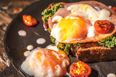 Toasted toast with bacon, poached egg, cherry tomatoes and lettuce on a black mica plate on a dark...