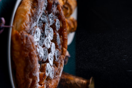 Banana Tarte Tatin is sprinkled with powdered sugar on a white plate on a dark background. The powder is poured onto the cake. Vertical Photo.の写真素材