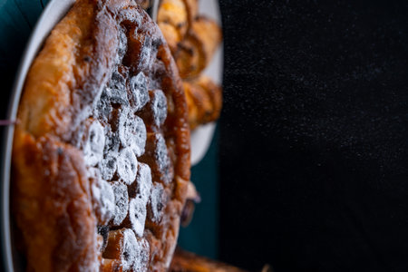 Banana Tarte Tatin is sprinkled with powdered sugar on a white plate on a dark background. The powder is poured onto the cake. Vertical Photo. High quality photoの写真素材