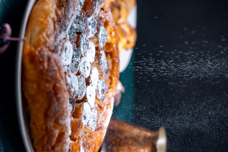 Banana Tarte Tatin is sprinkled with powdered sugar on a white plate on a dark background. The powder is poured onto the cake. Vertical Photo. High quality photoの写真素材