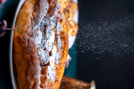 Banana Tarte Tatin is sprinkled with powdered sugar on a white plate on a dark background. The powder is poured onto the cake. Vertical Photo. High quality photoの写真素材