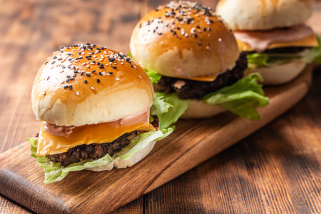 Three burgers with patty, cheese and lettuce on a wooden board and background. Close-up. Space for text. High quality photoの写真素材