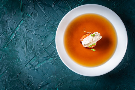 Soup or consomme, thick meat broth with carrots, chicken dumplings and microgreens, served in a white plate on a dark green background. View from above. Flat lay. High quality photoの写真素材