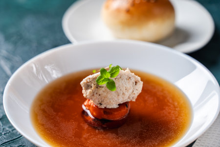 Soup or consomme, thick meat broth with carrots, chicken dumplings served in a white plate on a dark...