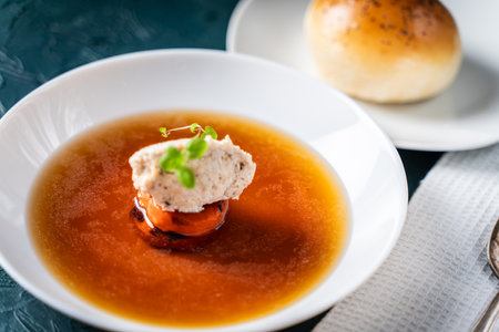 Soup or consomme, thick meat broth with carrots, chicken dumplings served in a white plate on a dark green background with sesame seed buns. High quality photoの写真素材