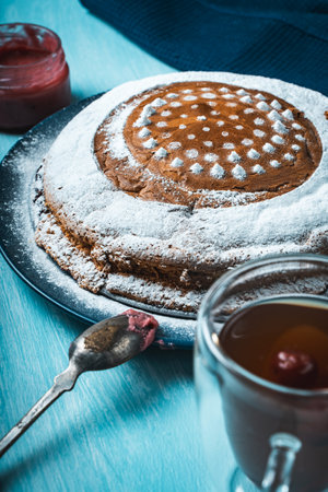 Homemade cake sprinkled with powdered sugar on a light blue background with a blue napkin and a cup of tea on the table. High quality photoの写真素材