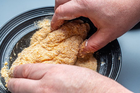 The cook's hands envelop the chicken breast in breadcrumbs. The process of preparing a traditional French recipe. High quality photoの写真素材