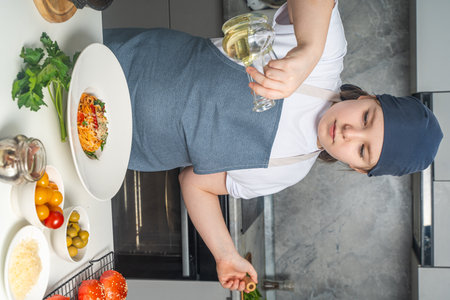 Little girl in apron cooking spaghetti in kitchen at home, pouring olive oil over cooked pasta in plate on white table. High quality photoの写真素材