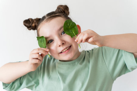 Cute little girl holding spinach leaves in her hands. High quality photo