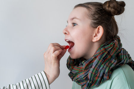 A little girl with a sore throat takes a pill. Mom's hand gives the pill to the girl. High quality photoの写真素材