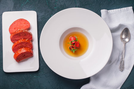 Consomme or broth with red omelette rolls served in a white plate with a red sesame bun on a dark green background with a napkin and spoon. Top view. Flat lay. High quality photoの写真素材