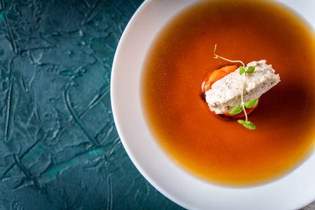 Soup or consomme, thick meat broth with carrots, chicken dumplings and microgreens, served in a white plate on a dark green background. View from above. Space for text. Flat lay. High quality photoの写真素材