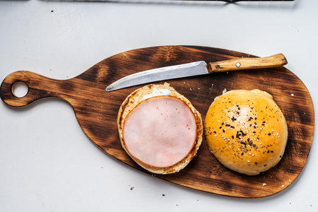 Sesame Bun Cut to Make Ham and Cheese Sandwich on Wooden Cutting Board with Knife on Gray Background. High quality photoの写真素材
