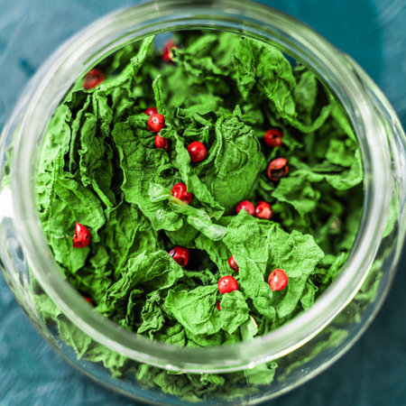 Dried basil leaves and pink pepper in a glass jar on a malachite background. Close-up. View from...