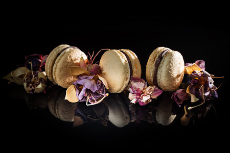 Cream-colored French macarons with flowers on a black background with reflection. Original serving of the dessert. High quality photoの写真素材