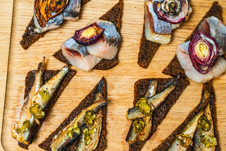 Rye toast bread with herring and sprats, with onions and potatoes on a wooden board. Norwegian cuisine. High quality photoの写真素材