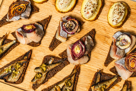 Rye toast bread with herring and sprats, with onions and potatoes on a wooden board. Norwegian cuisine. High quality photoの写真素材