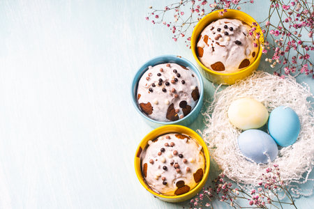 Delicious Easter cupcakes and eggs on a light blue background with flowers. Easter cakes with glaze in bright baking molds of yellow and sky color. Copy space. High quality photoの写真素材