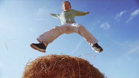 Happy little girl jumping in the air over a haystack against a blue sky. The concept of a happy and...