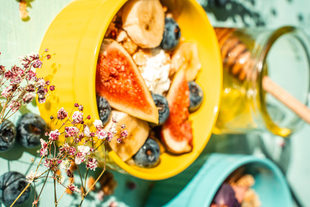 Granola with fresh banana, figs and blueberries on a light table with honey and flowers in a yellow and blue bowl. The concept of a delicious and healthy breakfast, a good start to the day. High quality photoの写真素材