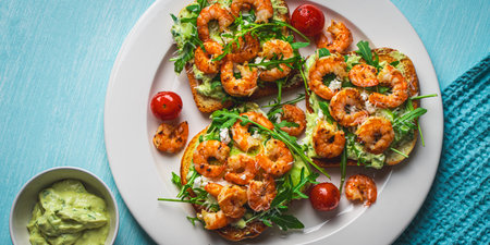 Toast or sandwiches with avocado oil, arugula and fried prawns on a white plate on a light blue background with a napkin. Healthy breakfast. View from above. Flat layout. Space for text. High quality photoの写真素材