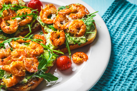 Toast or sandwiches with avocado oil, arugula and fried prawns on a white plate on a light blue background with a napkin. Healthy breakfast. View from above. Flat layout. Space for text. High quality photoの写真素材