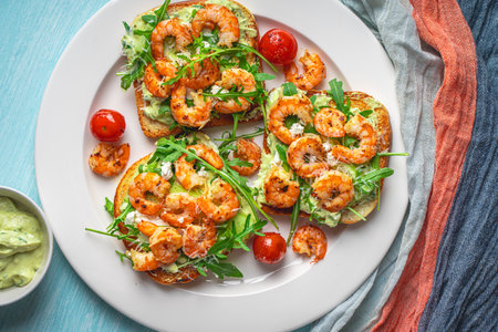 Toast or sandwiches with avocado oil, arugula and fried prawns on a white plate on a light blue background with a napkin. Healthy breakfast. View from above. Flat layout. Space for text. High quality photoの写真素材