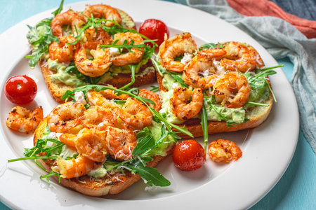 Toast with shrimp, avocado and arugula with tomatoes on a white plate on a blue background with a napkin. The concept of a healthy breakfast. Close-up. High quality photoの写真素材