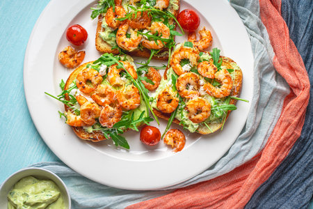 Toast with shrimp, avacado and arugula with tomatoes on a white plate on a blue background with a napkin. The concept of a healthy breakfast. Close-up. High quality photoの写真素材