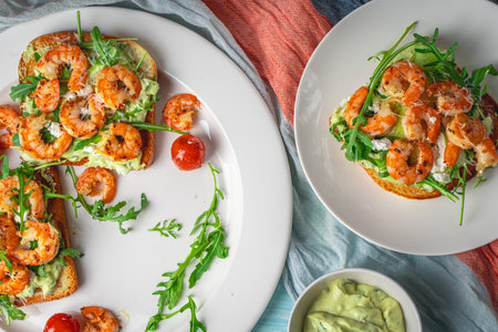 Toast with shrimp, avacado and arugula with tomatoes on a white plate on a blue background with a napkin. The concept of a healthy breakfast. Close-up. High quality photoの写真素材