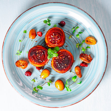 Carrot dessert, slices of carrots wrapped in a roll, fried and poured with honey with kumquat and cranberries on a blue plate. Healthy dessert. View from above. High quality photoの写真素材
