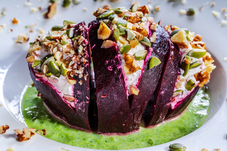 Beetroot with cottage cheese cream, nuts and pumpkin seeds on green spinach sauce is served on a white plate. Restaurant serving of a healthy dish. Close-up. High quality photoの写真素材