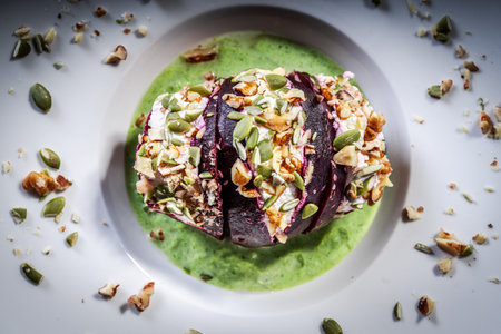 Beetroot with cottage cheese cream, nuts and pumpkin seeds on green spinach sauce served on a white plate. Restaurant serving of a healthy dish. Top view. High quality photoの写真素材