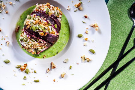 Beetroot with cottage cheese cream, nuts and pumpkin seeds on green spinach sauce served on a white...