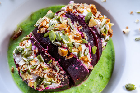 Beetroot with cottage cheese cream, nuts and pumpkin seeds on green spinach sauce served on a white plate. Concept healthy food - beautiful. Restaurant serving. Close-up. Top view. High quality photoの写真素材
