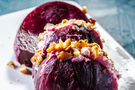 Pieces of beetroot stuffed with cream cheese and nuts on a white plate with pumpkin seeds on a green...