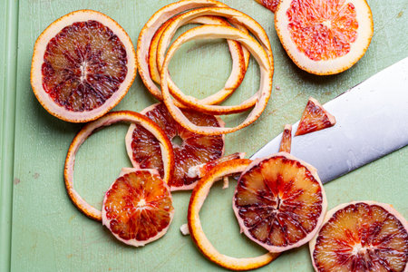 Blood oranges are cut with a knife on a green cutting board. High quality photo