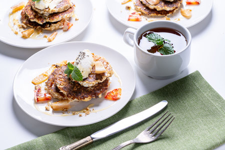 Cottage cheese pancakes with orange and chia seeds on a white plate with a cup of tea and mint on a light background. The concept of a healthy, dietary breakfast at home. High quality photoの写真素材