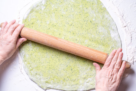 Women's hands roll out green dough with spinach with a rolling pin. The concept of healthy eating. Top view. High quality photoの写真素材