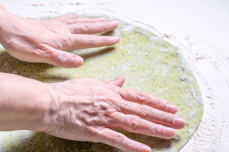 Women's hands roll out green dough with spinach with a rolling pin. The concept of healthy eating. Top view. High quality photoの写真素材