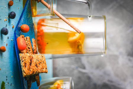 Crackers with flax seeds, nuts and sesame seeds on a blue plate and tea with lemon and honey on the table on a gray background. High quality photoの写真素材